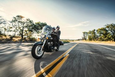 Couple riding on Kawasaki Vulcan 900 Classic LT down sunny rural road